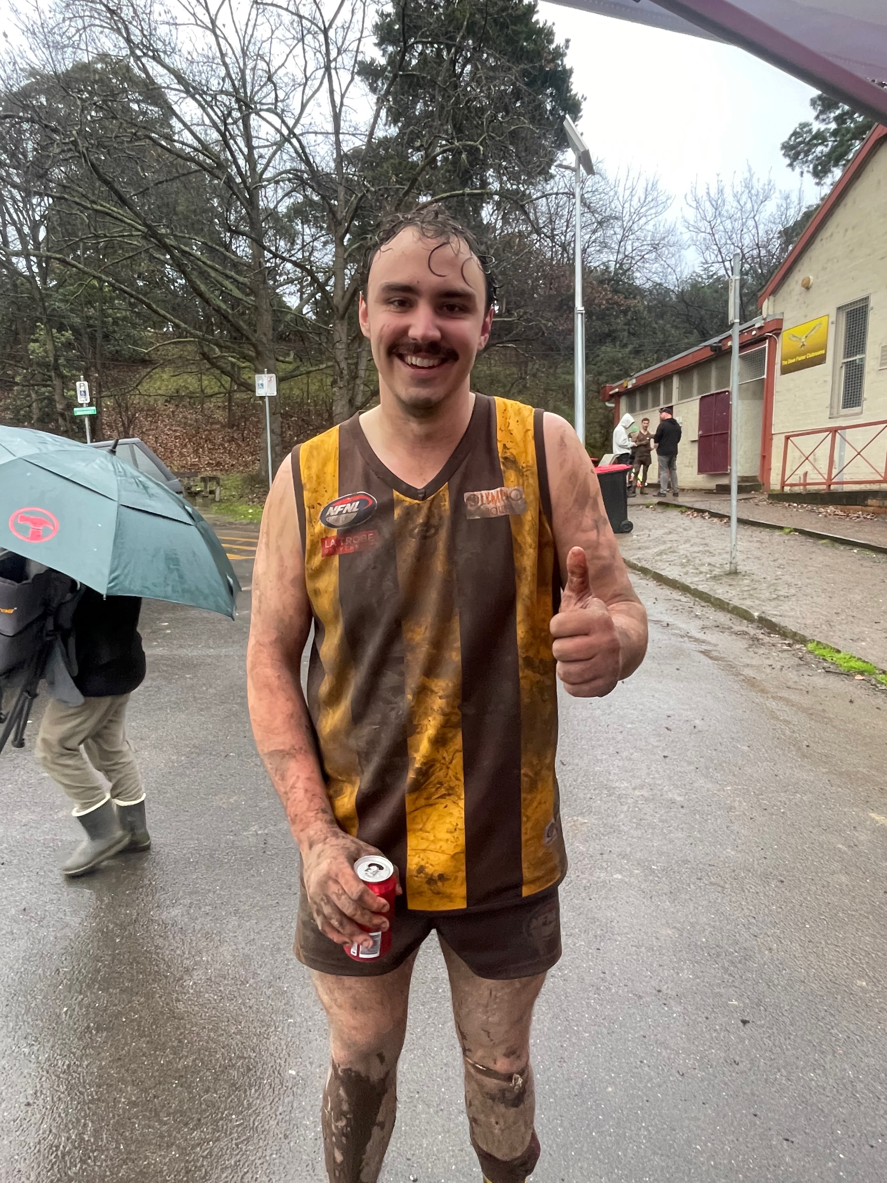 Pat post-match, mud-covered in brown and gold guernsey, smiling with a thumbs up
